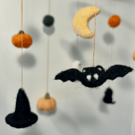 Close up of a Halloween baby mobile’s hanging items with pumpkins, a bat, a witch’s hat, a crescent moon, and orange and green balls.