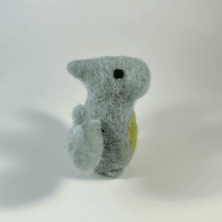A needle-felted grey blue pterodactyl with a green tummy faces towards the right.